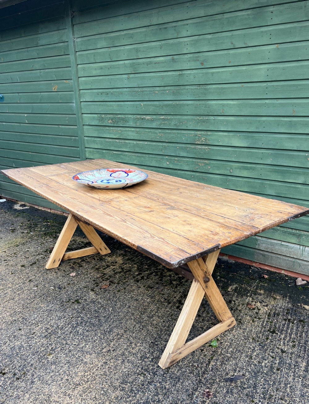 An early 20th-century long pine tavern table with angled trestle legs and protective metal corner brackets.