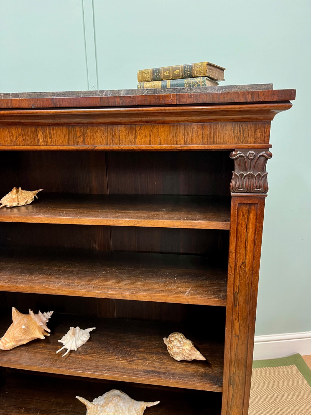 A George IV open rosewood dwarf bookcase featuring carved acanthus pilasters, four open shelves, and a grey marble top. View II