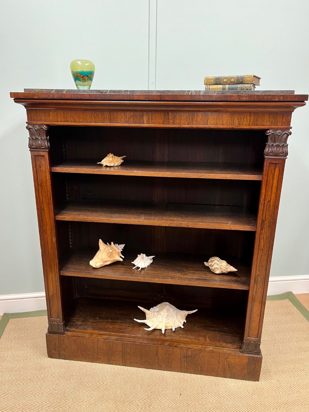 A George IV open rosewood dwarf bookcase featuring carved acanthus pilasters, four open shelves, and a grey marble top.