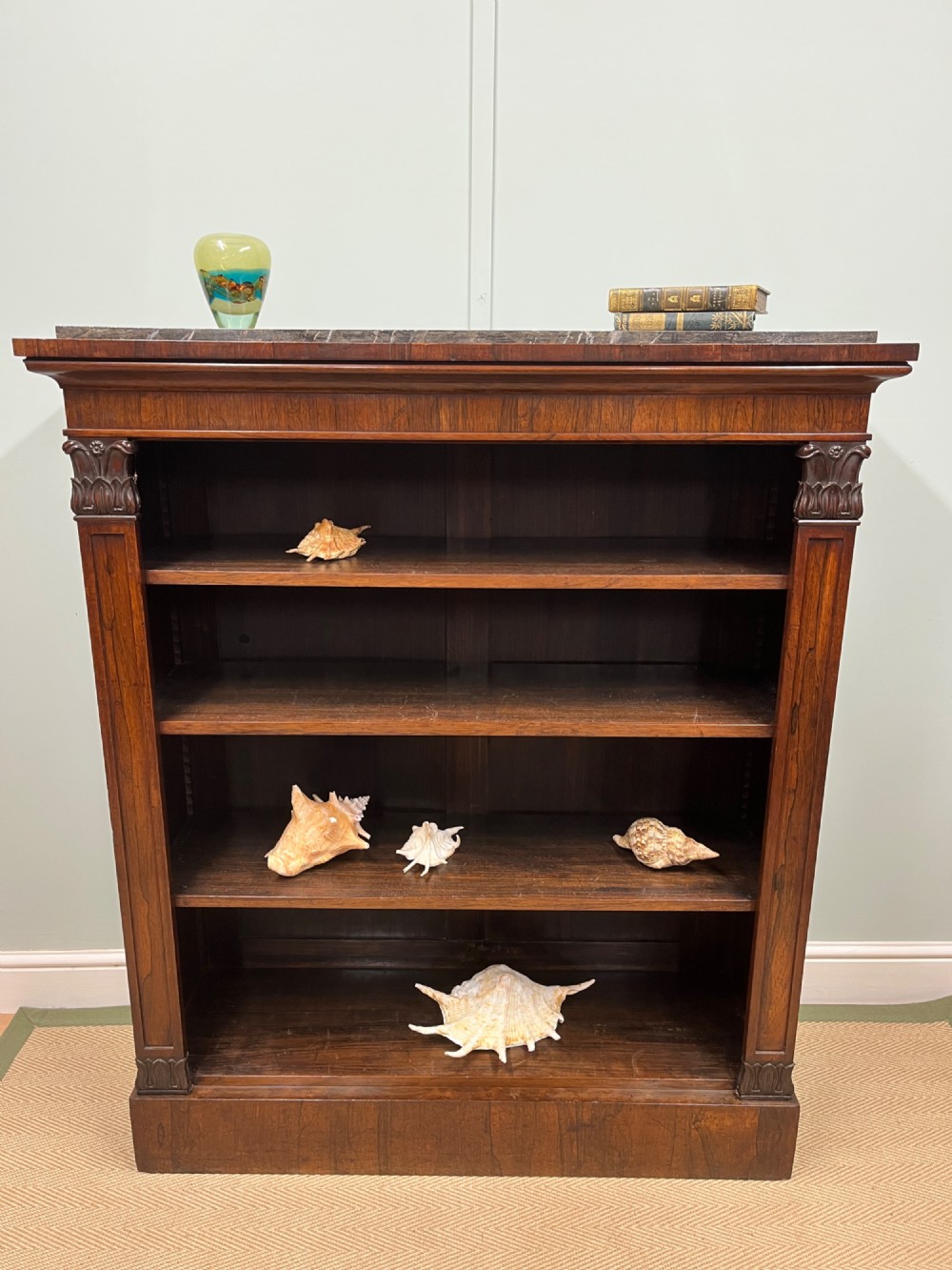 A George IV open rosewood dwarf bookcase featuring carved acanthus pilasters, four open shelves, and a grey marble top. View IV