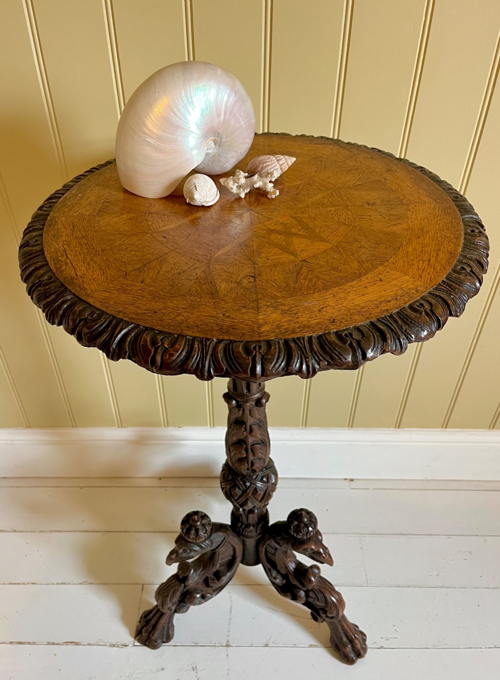 A 19th-century French oak round side table featuring a geometric parquetry top, carved rim, turned column pedestal, and carved tripod feet.