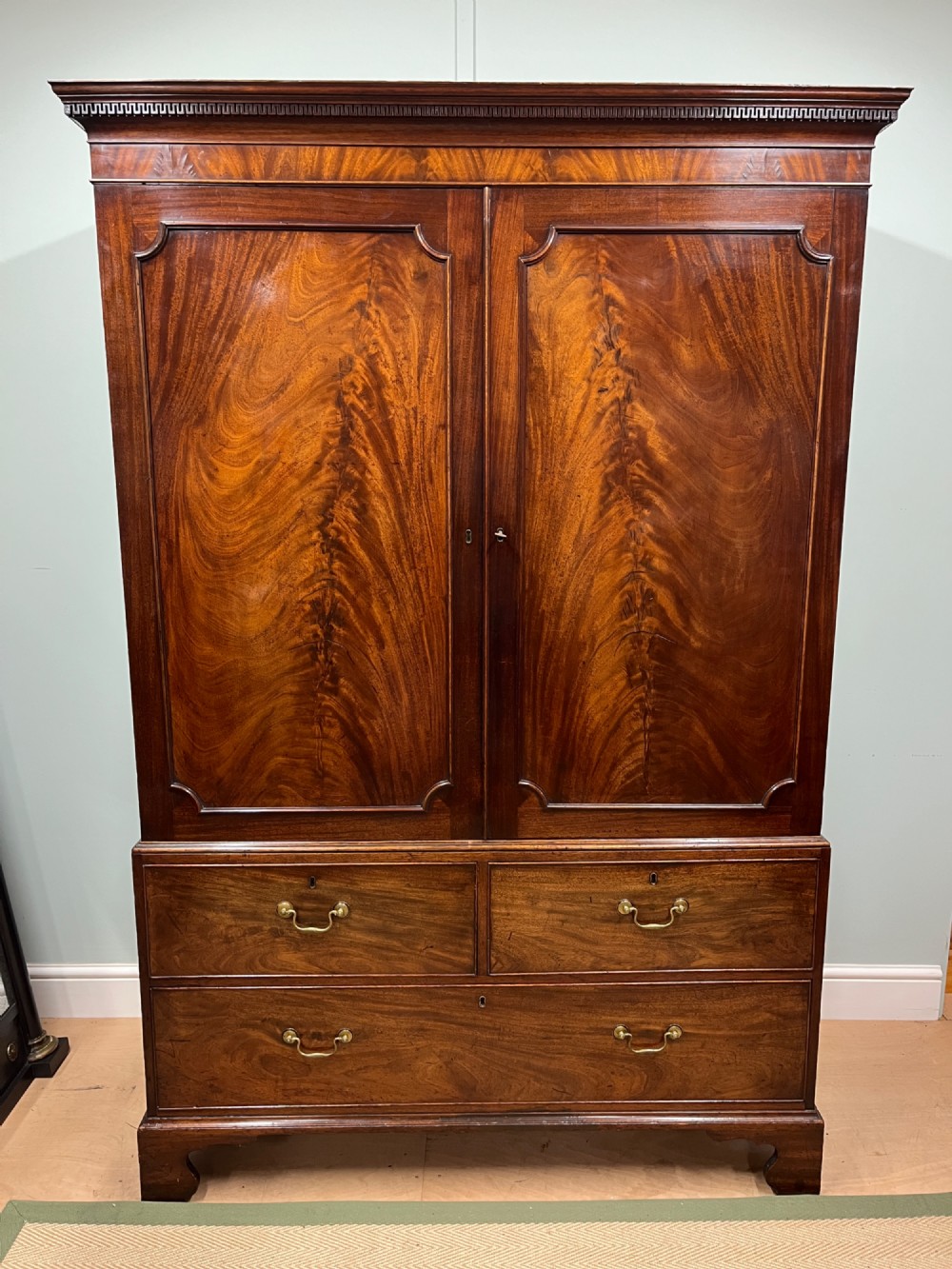 A nineteenth-century flame mahogany linen press featuring panelled cupboard doors above three lower drawers with brass swan-neck handles.