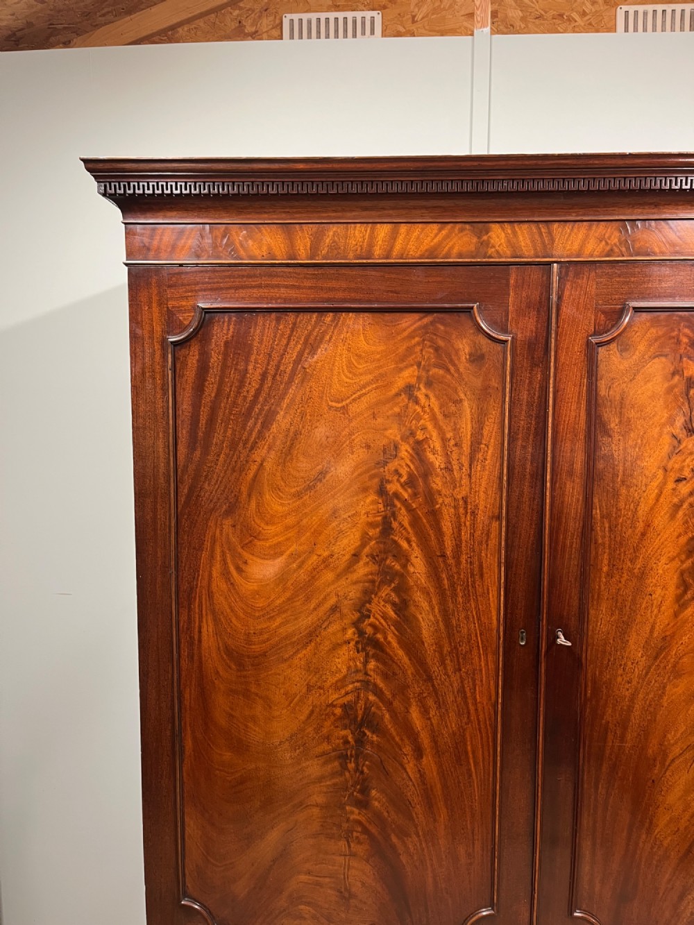 A nineteenth-century flame mahogany linen press featuring panelled cupboard doors above three lower drawers with brass swan-neck handles. View III