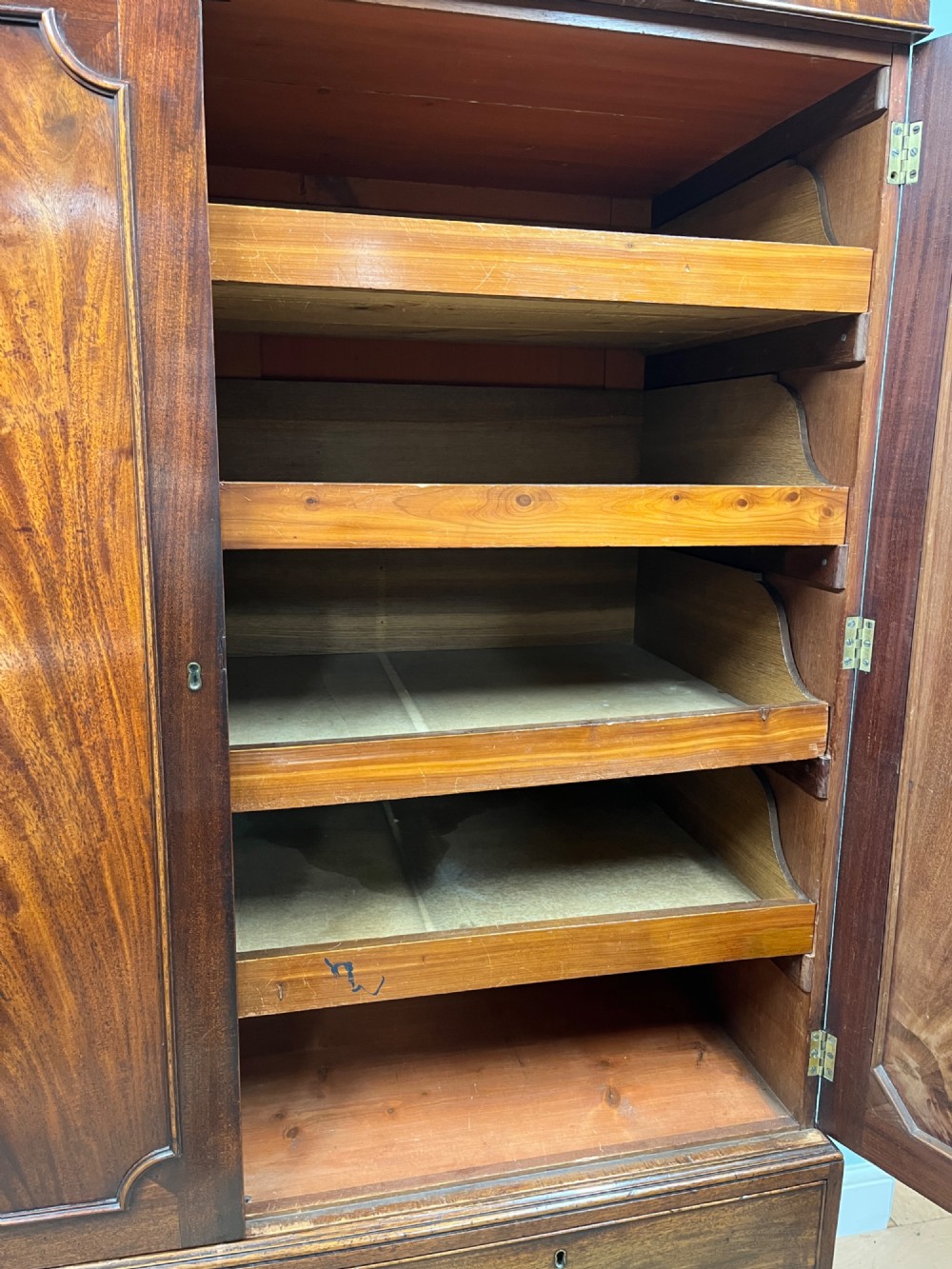 A nineteenth-century flame mahogany linen press featuring panelled cupboard doors above three lower drawers with brass swan-neck handles. View V
