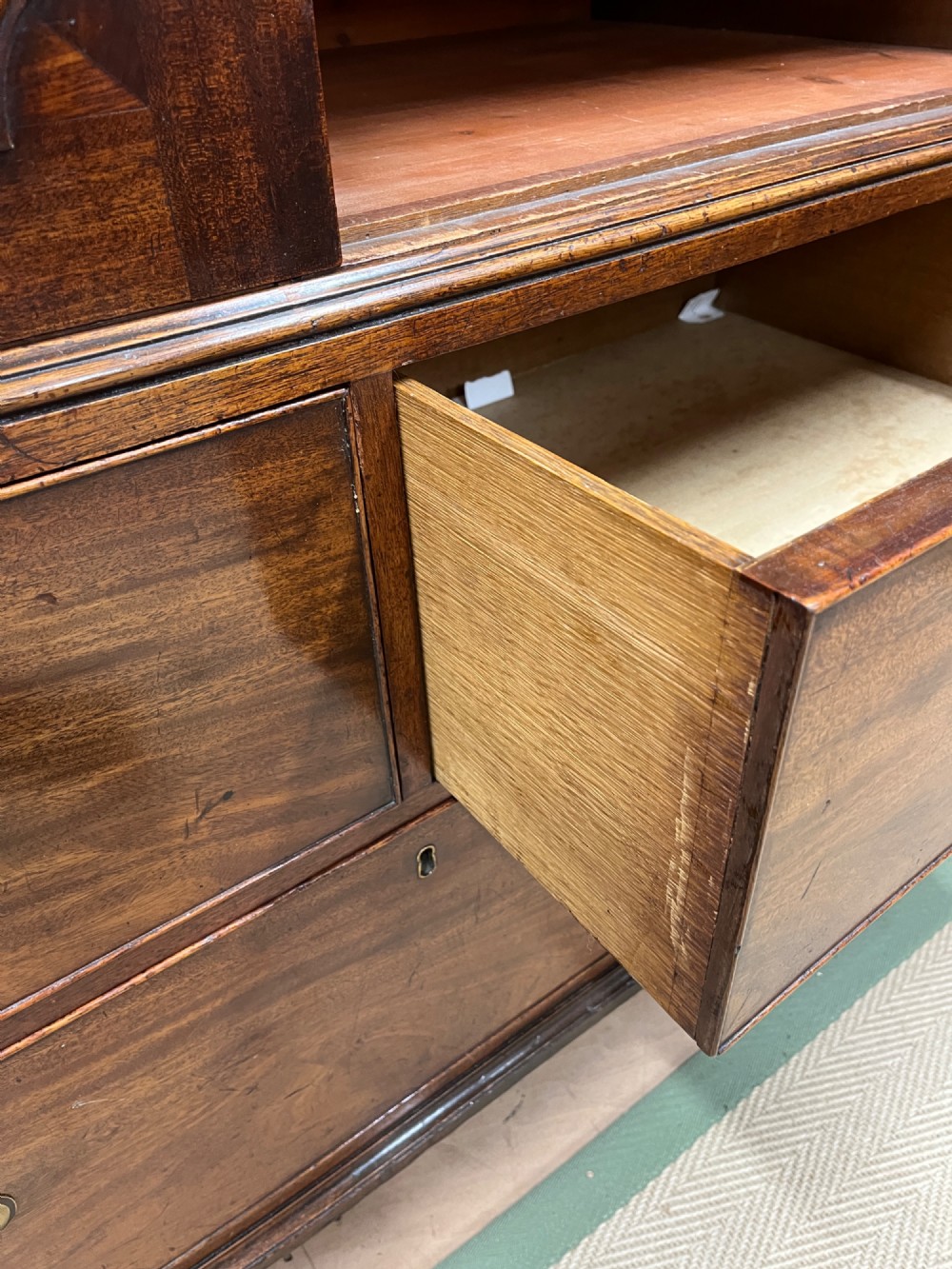 A nineteenth-century flame mahogany linen press featuring panelled cupboard doors above three lower drawers with brass swan-neck handles. View VI