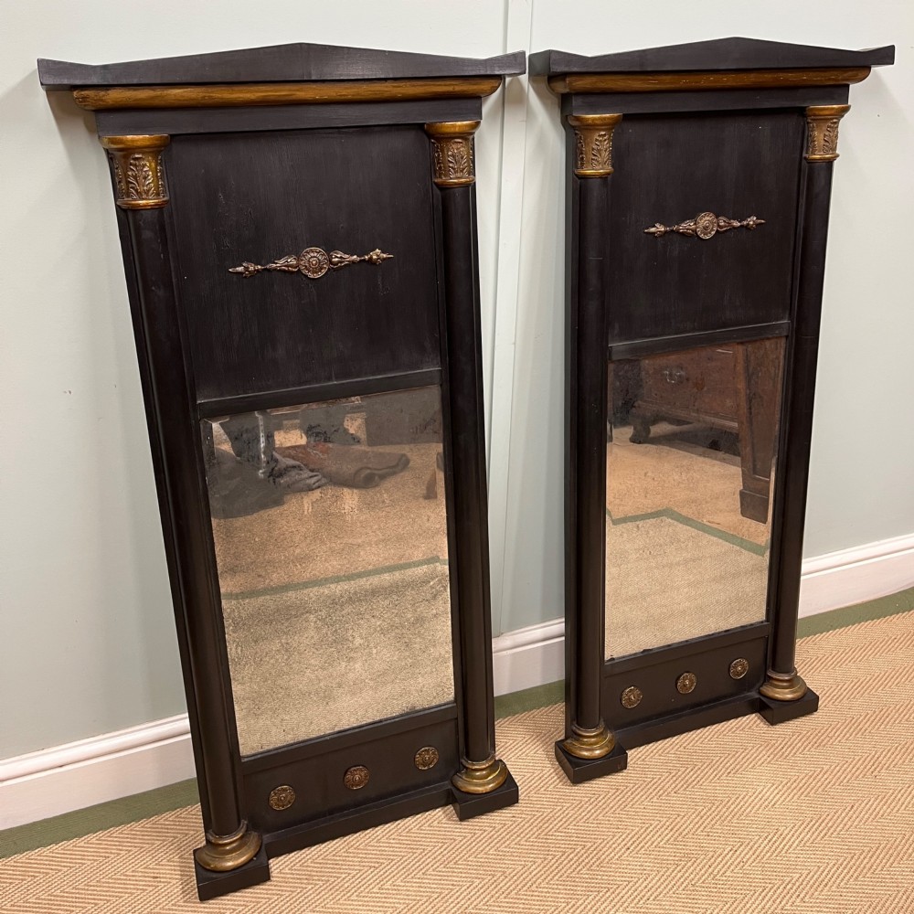 A pair of tall Empire style ebonised pier mirrors featuring gilt column capitals, architectural tops, and classical metal appliques. View II