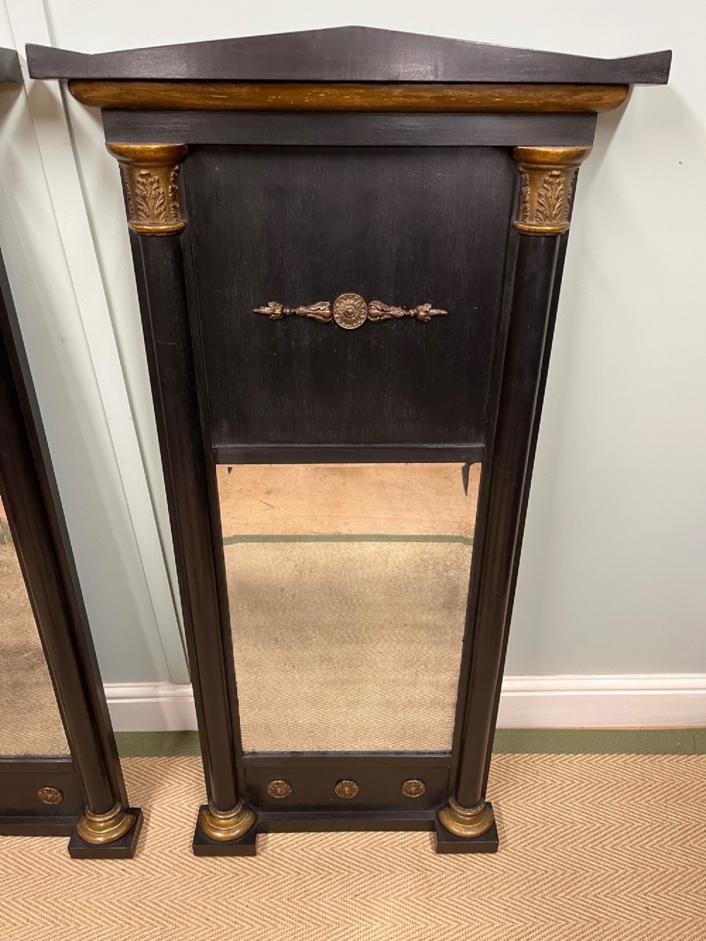A pair of tall Empire style ebonised pier mirrors featuring gilt column capitals, architectural tops, and classical metal appliques. View III