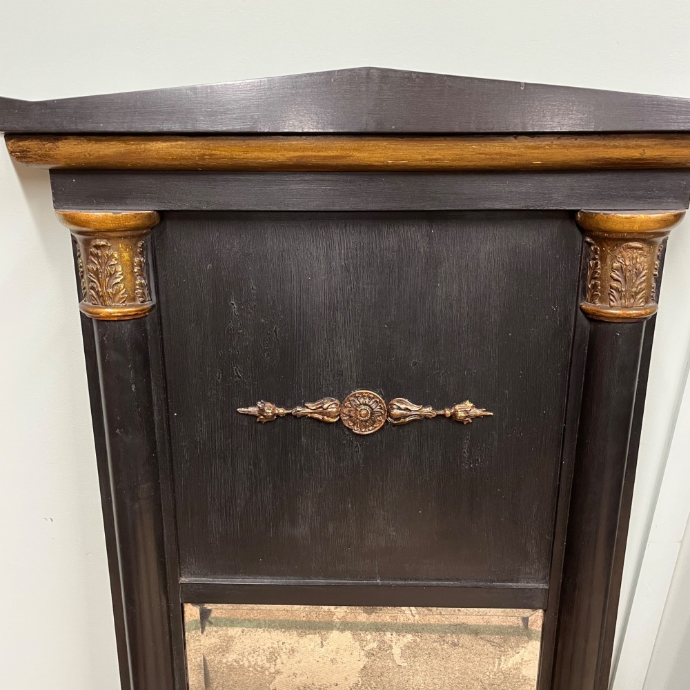 A pair of tall Empire style ebonised pier mirrors featuring gilt column capitals, architectural tops, and classical metal appliques. View IV