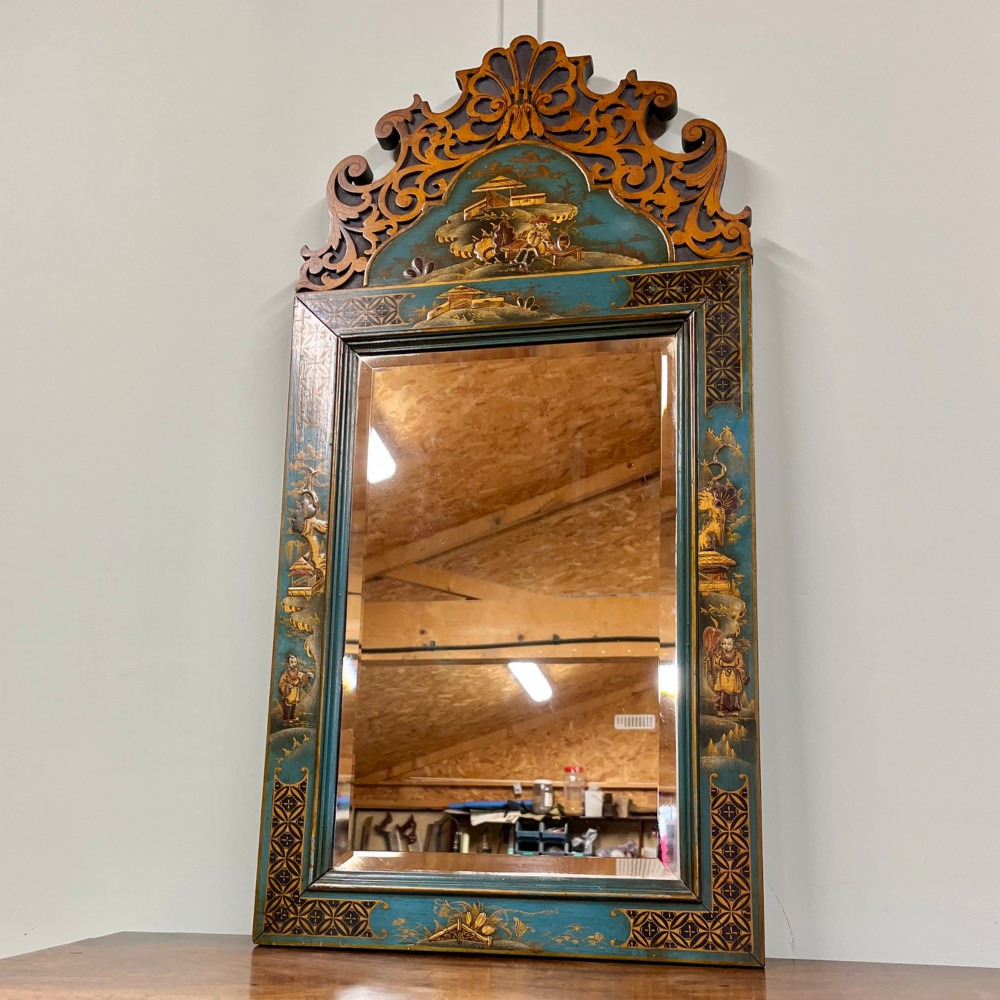 An Edwardian Chinoiserie wall mirror featuring a teal blue and gilt painted wooden frame with hand-painted Asian landscapes and a carved openwork cresting.