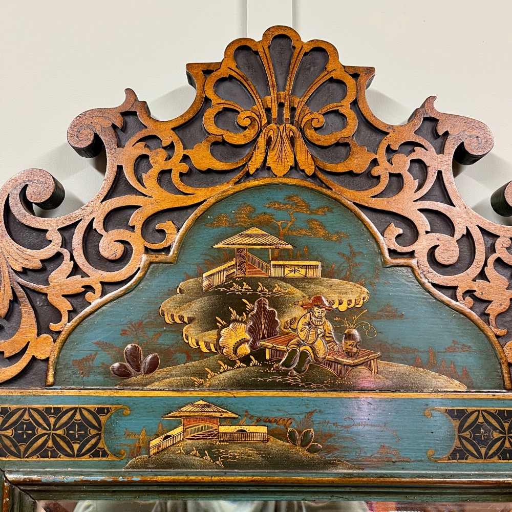 An Edwardian Chinoiserie wall mirror featuring a teal blue and gilt painted wooden frame with hand-painted Asian landscapes and a carved openwork cresting. View II