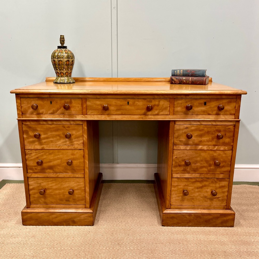 A 19th-century satin birch twin-pedestal desk featuring nine drawers with turned wooden knobs and a low gallery back.