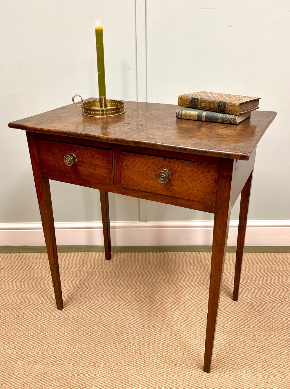 A 19th-century burr ash side table featuring two front drawers with round brass knobs and slender tapered square legs.