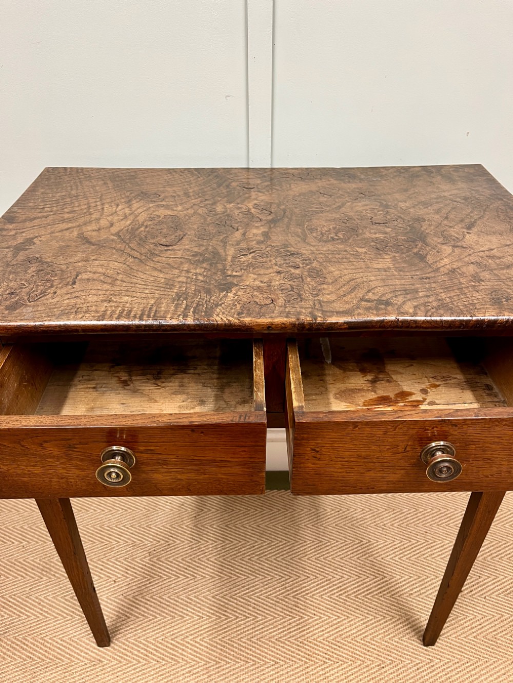 A 19th-century burr ash side table featuring two front drawers with round brass knobs and slender tapered square legs. View V