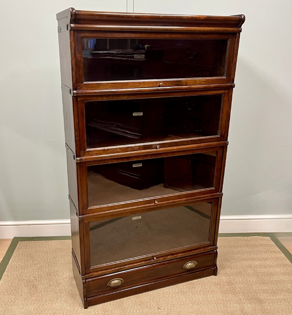 An Edwardian Globe Wernicke four-section dark mahogany barrister bookcase featuring glazed lifting doors, brass handles, and a base drawer.