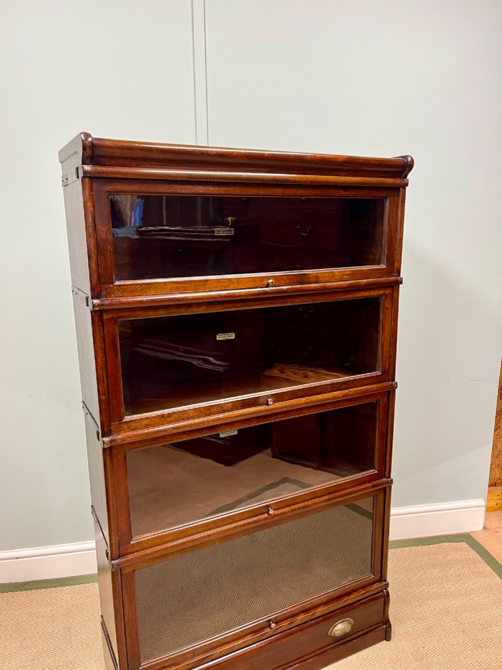 An Edwardian Globe Wernicke four-section dark mahogany barrister bookcase featuring glazed lifting doors, brass handles, and a base drawer. View II