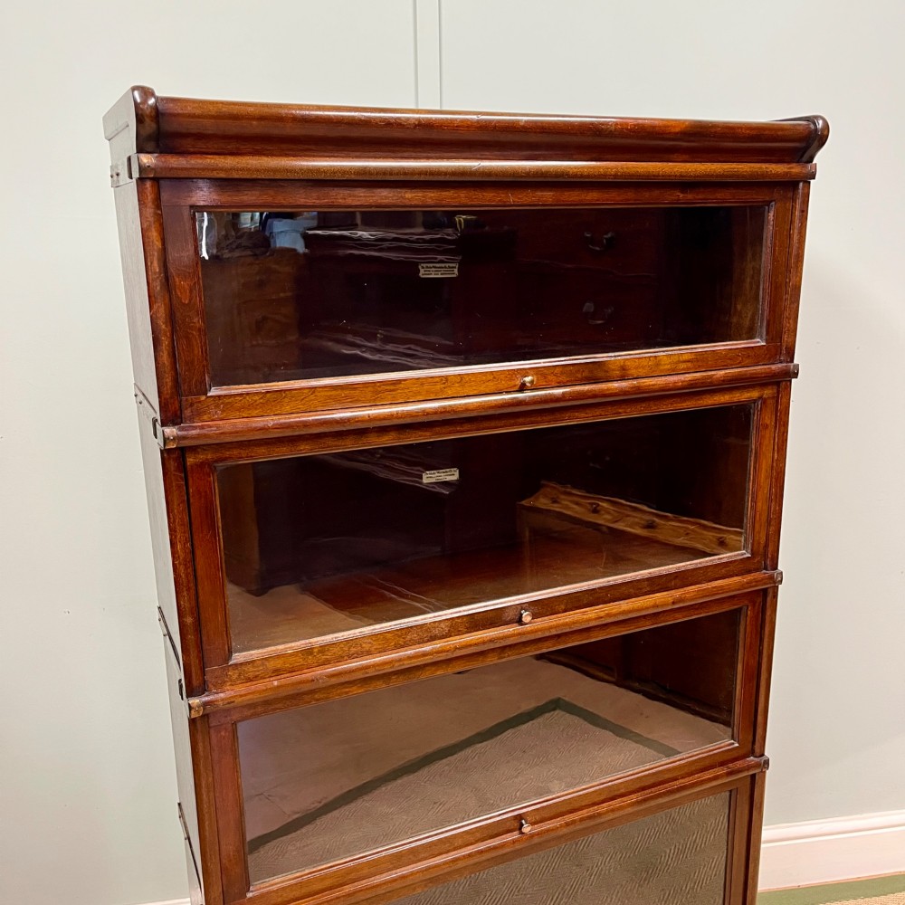 An Edwardian Globe Wernicke four-section dark mahogany barrister bookcase featuring glazed lifting doors, brass handles, and a base drawer. View III