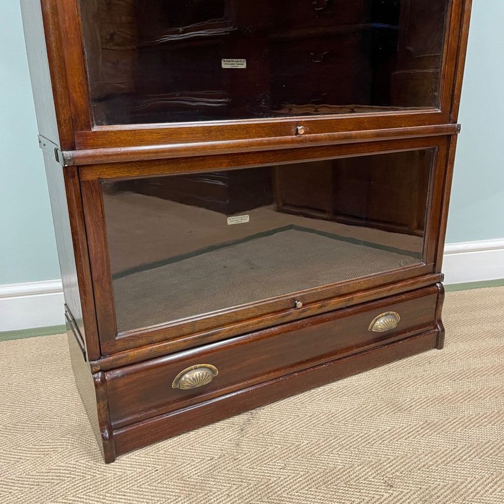 An Edwardian Globe Wernicke four-section dark mahogany barrister bookcase featuring glazed lifting doors, brass handles, and a base drawer. View IV