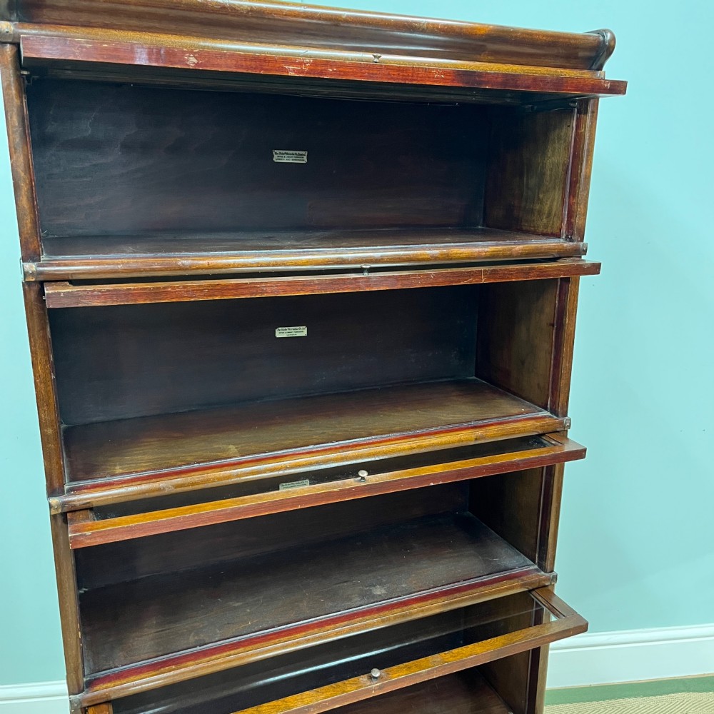 An Edwardian Globe Wernicke four-section dark mahogany barrister bookcase featuring glazed lifting doors, brass handles, and a base drawer. View VI