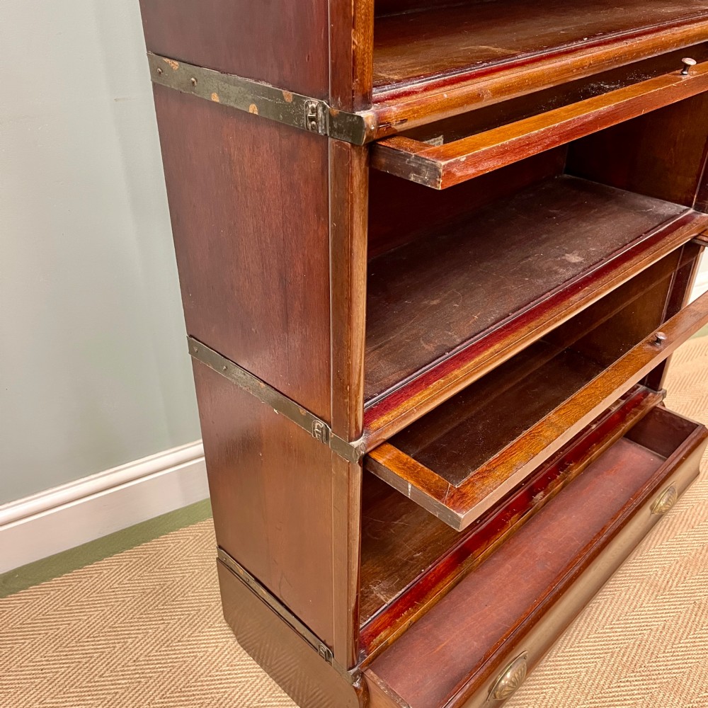 An Edwardian Globe Wernicke four-section dark mahogany barrister bookcase featuring glazed lifting doors, brass handles, and a base drawer. View IX