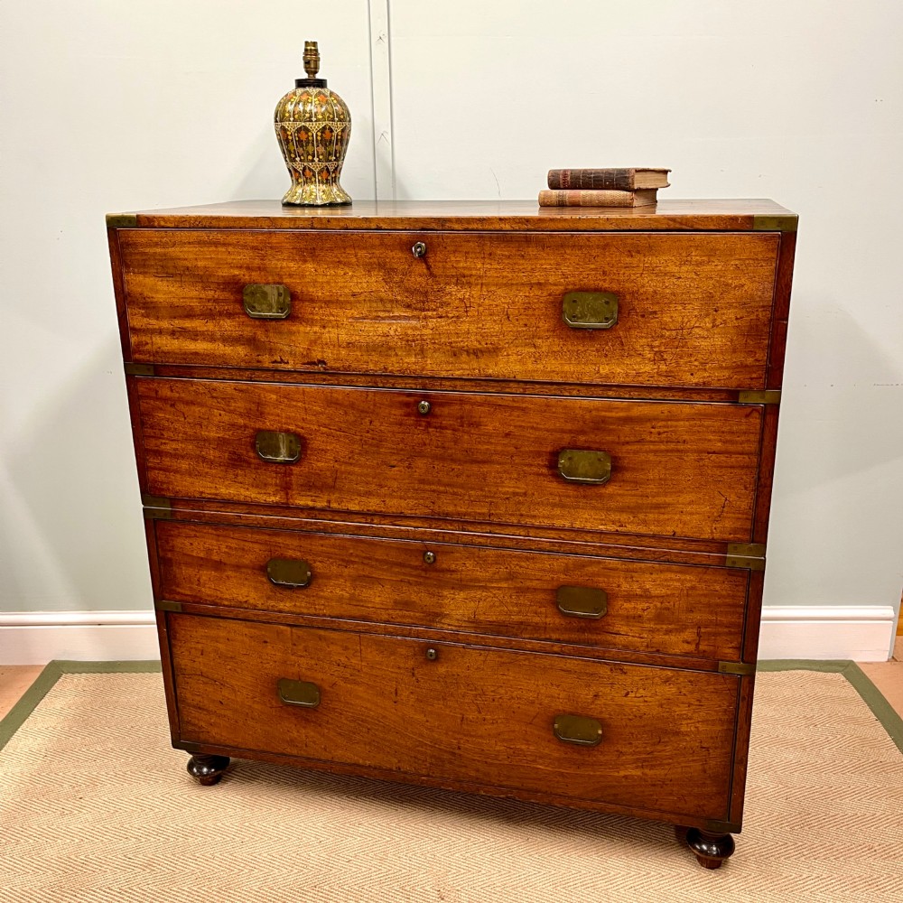 A 19th-century mahogany military campaign secretaire chest featuring four drawers with recessed brass handles and brass corner straps, resting on turned feet.
