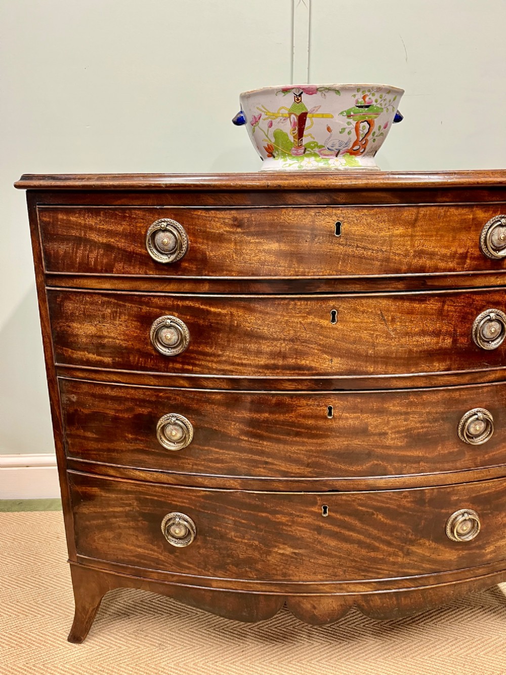 An antique Regency bow-fronted mahogany chest of drawers with four graduated drawers, brass ring handles, and splayed bracket feet. View II
