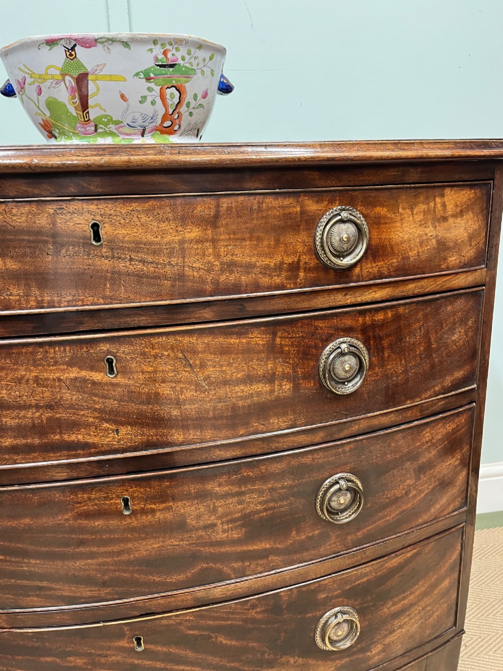 An antique Regency bow-fronted mahogany chest of drawers with four graduated drawers, brass ring handles, and splayed bracket feet. View III