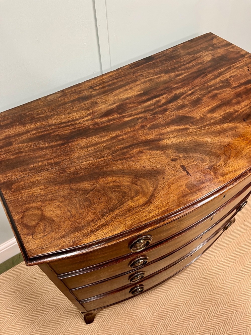 An antique Regency bow-fronted mahogany chest of drawers with four graduated drawers, brass ring handles, and splayed bracket feet. View VI