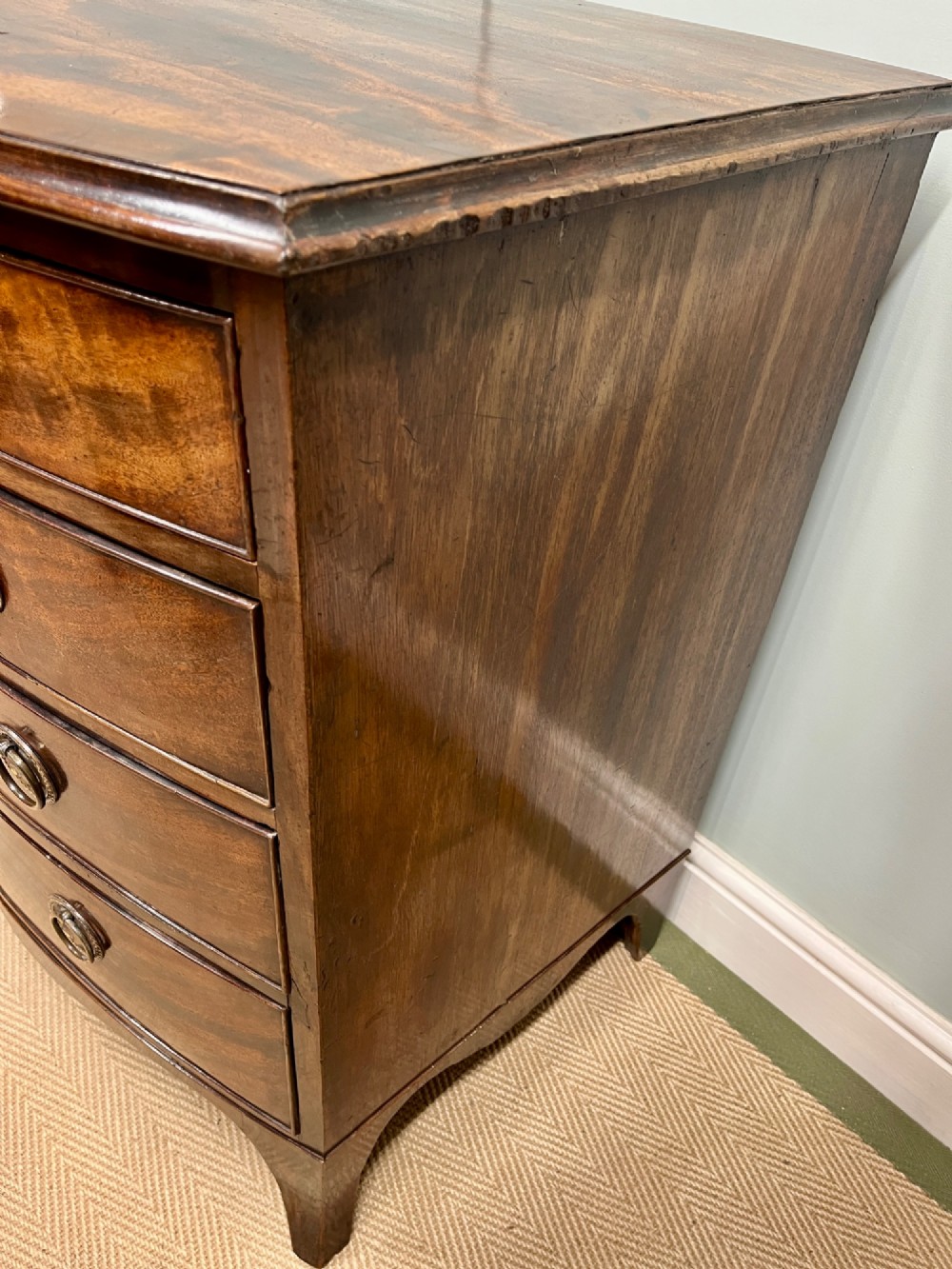 An antique Regency bow-fronted mahogany chest of drawers with four graduated drawers, brass ring handles, and splayed bracket feet. View VII