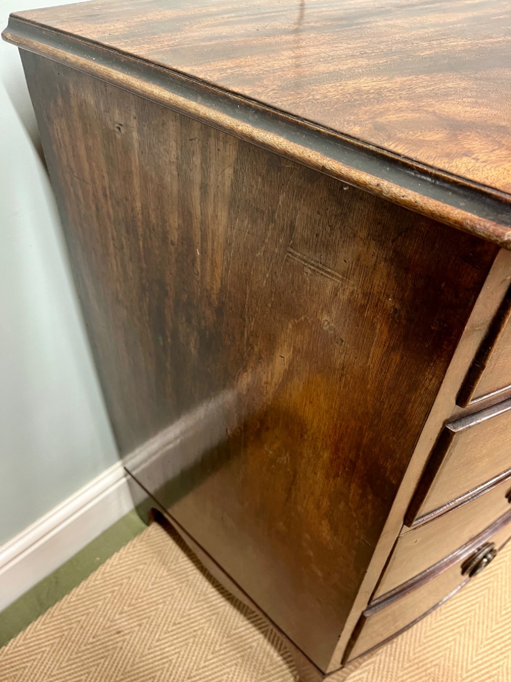 An antique Regency bow-fronted mahogany chest of drawers with four graduated drawers, brass ring handles, and splayed bracket feet. View VIII
