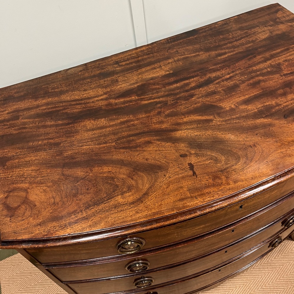 An antique Regency bow-fronted mahogany chest of drawers with four graduated drawers, brass ring handles, and splayed bracket feet. View IX