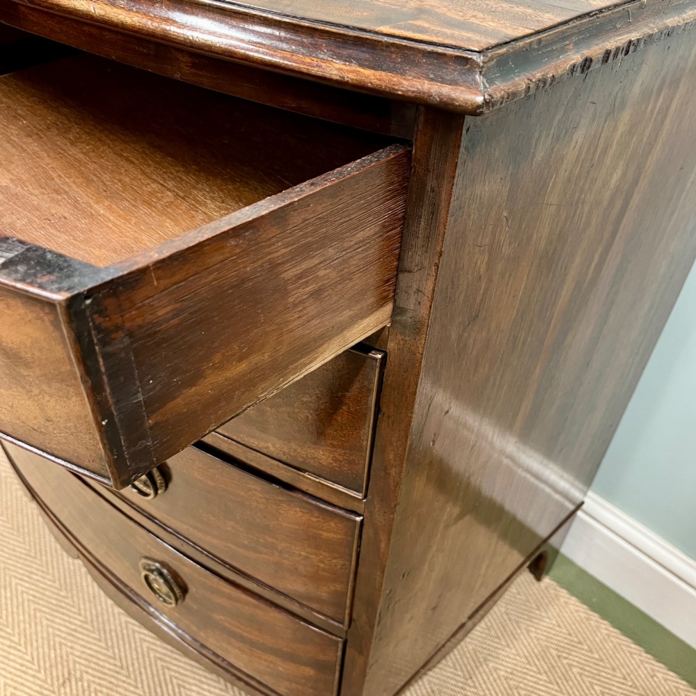An antique Regency bow-fronted mahogany chest of drawers with four graduated drawers, brass ring handles, and splayed bracket feet. View X
