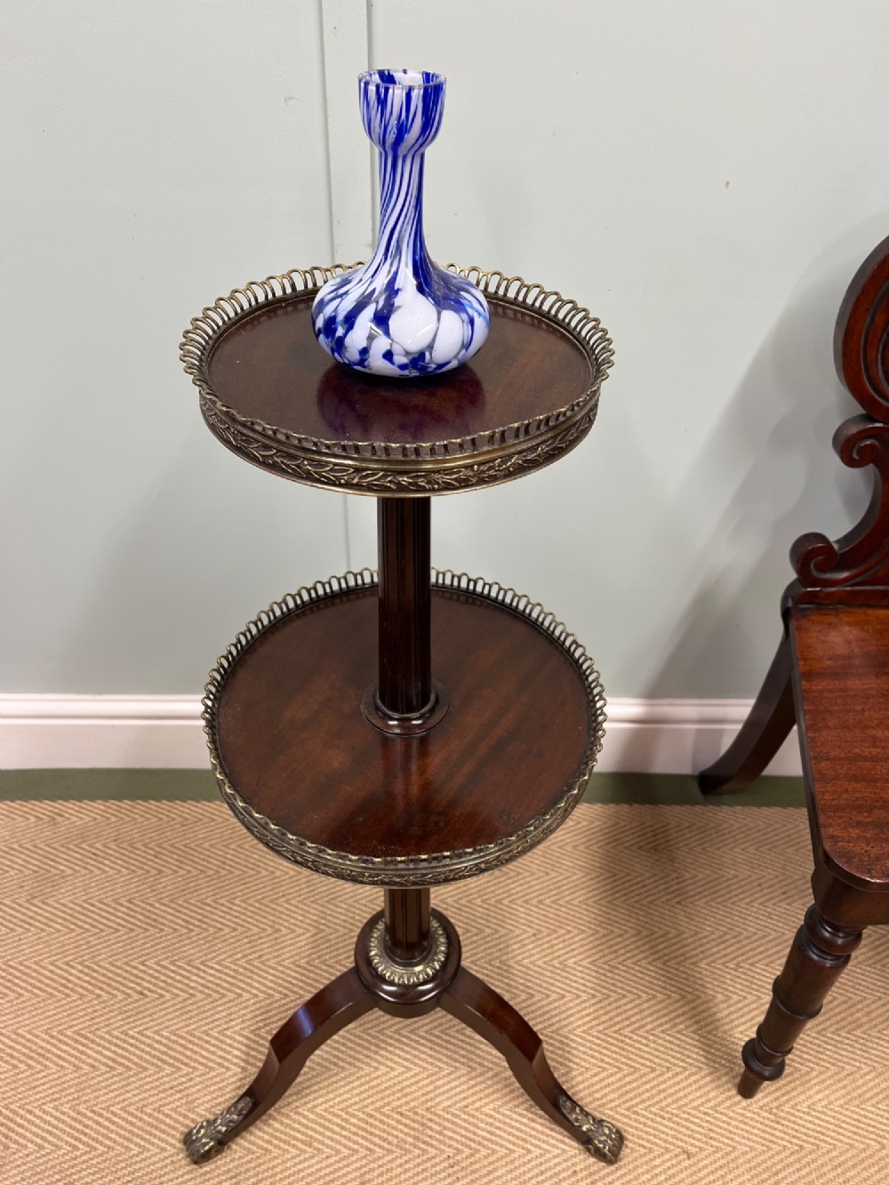 A two-tier dark mahogany dumb waiter featuring pierced brass galleries, a fluted central stem, and a tripod base with brass feet. View II
