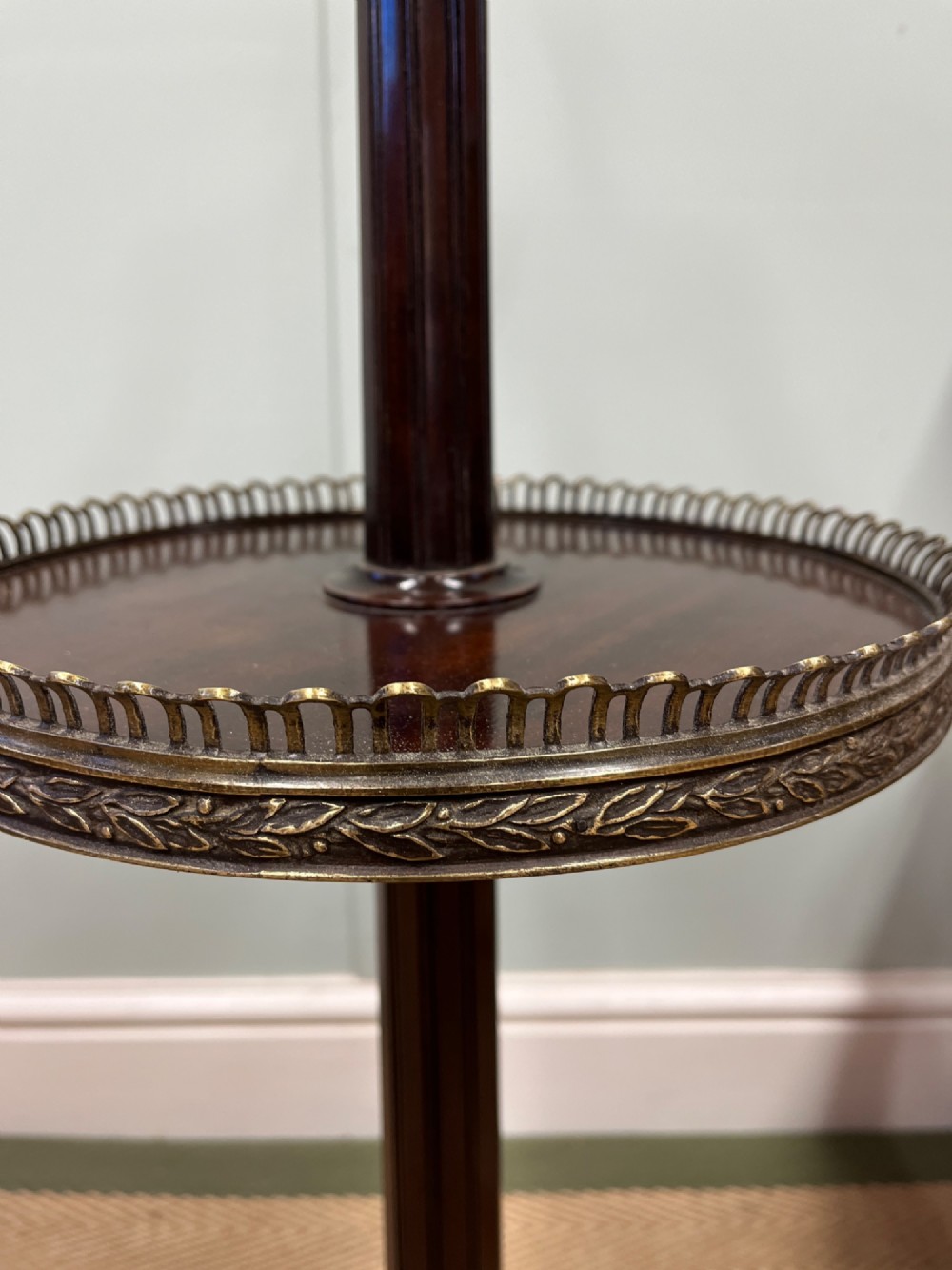 A two-tier dark mahogany dumb waiter featuring pierced brass galleries, a fluted central stem, and a tripod base with brass feet. View V