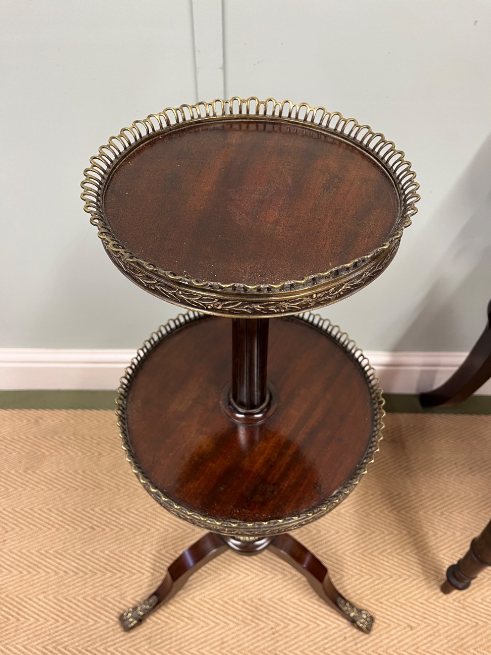 A two-tier dark mahogany dumb waiter featuring pierced brass galleries, a fluted central stem, and a tripod base with brass feet. View VI