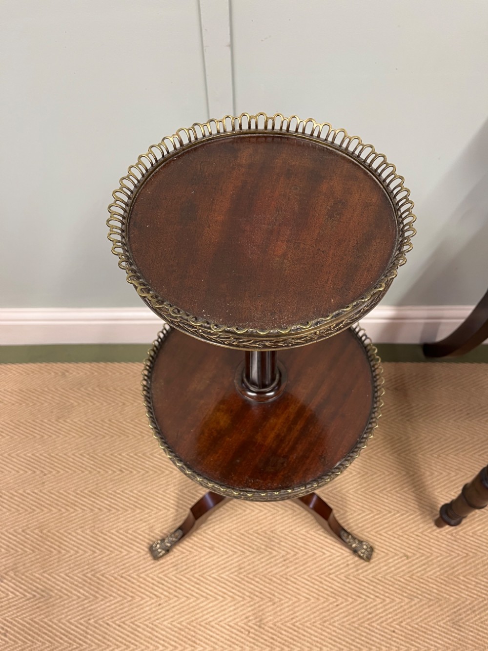 A two-tier dark mahogany dumb waiter featuring pierced brass galleries, a fluted central stem, and a tripod base with brass feet. View VII