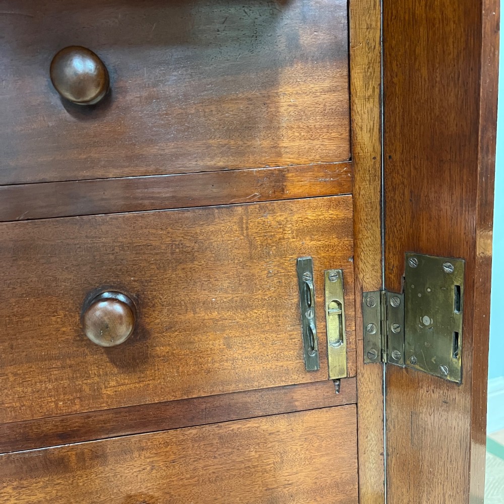 A tall Victorian mahogany Wellington chest featuring eight graduated drawers with turned wooden knobs, carved corbels at the top, and a side hinged locking flap on a plinth base. View V