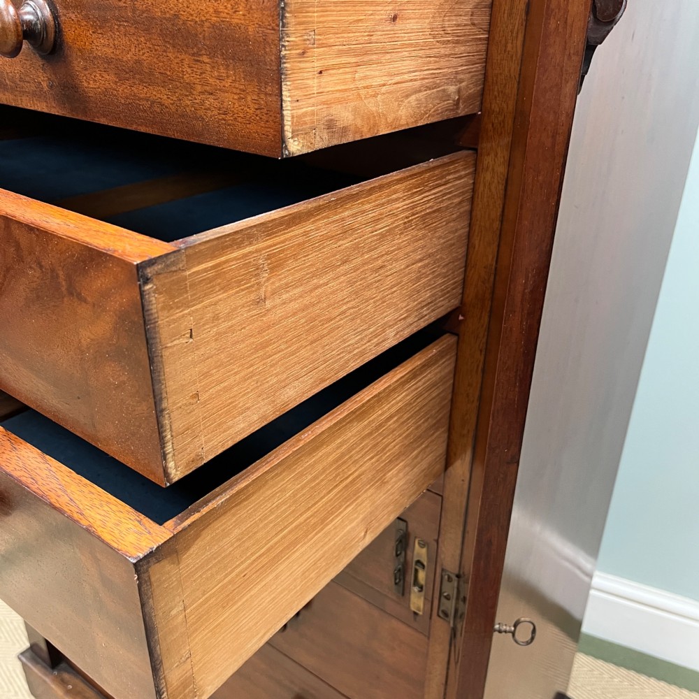 A tall Victorian mahogany Wellington chest featuring eight graduated drawers with turned wooden knobs, carved corbels at the top, and a side hinged locking flap on a plinth base. View VII
