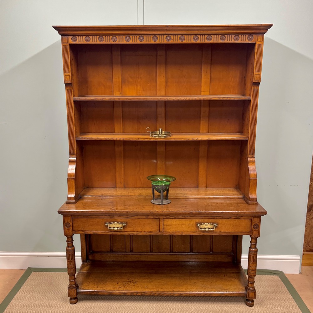 A 19th-century oak dresser featuring a three-tiered open shelf rack above two drawers with brass swan-neck handles and an open pot board base on turned legs.