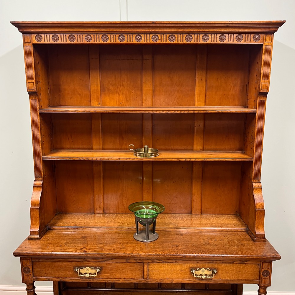 A 19th-century oak dresser featuring a three-tiered open shelf rack above two drawers with brass swan-neck handles and an open pot board base on turned legs. View XIII