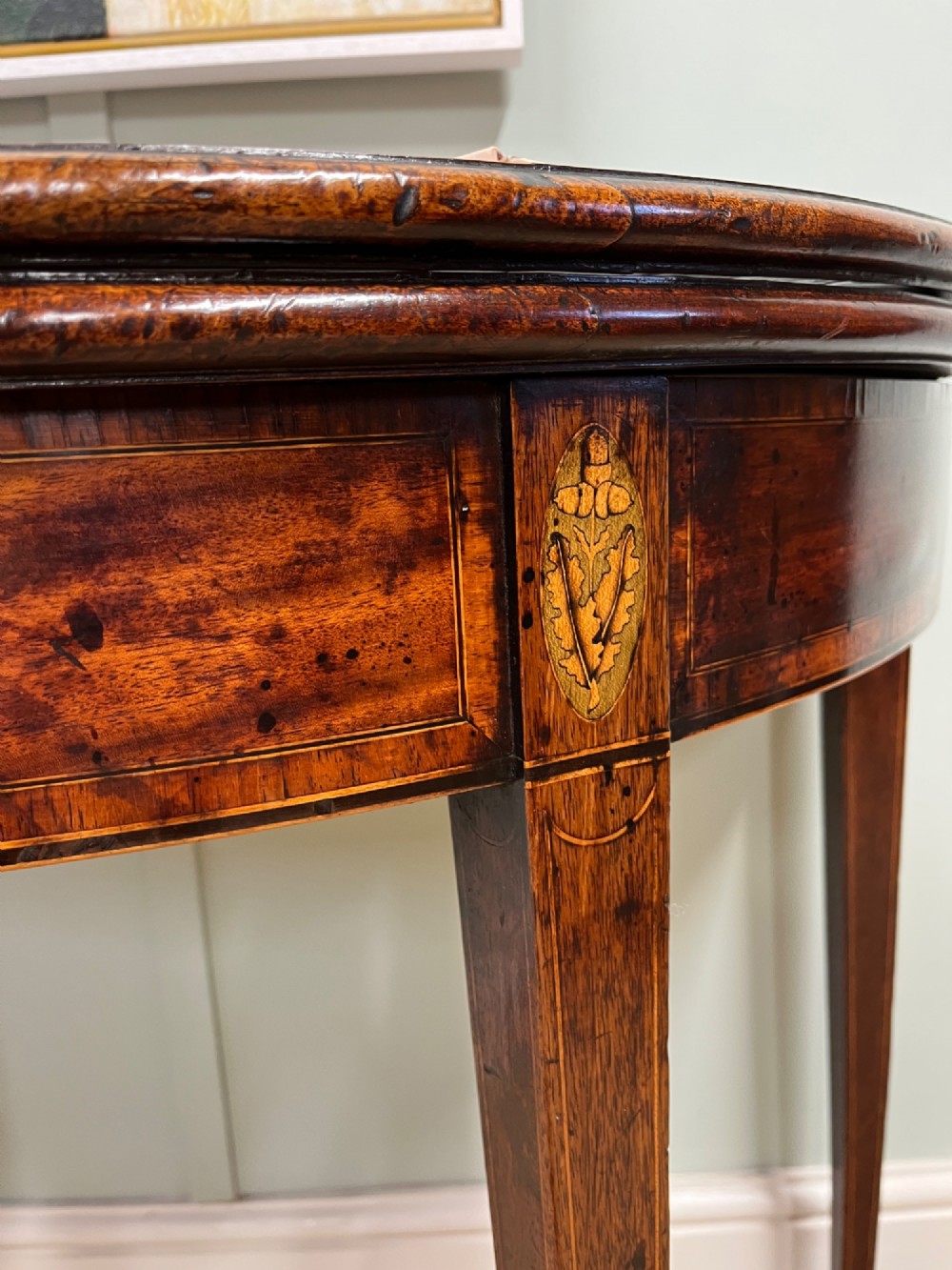 A Georgian mahogany demilune tea table featuring wood stringing and four tapered square legs. View IV