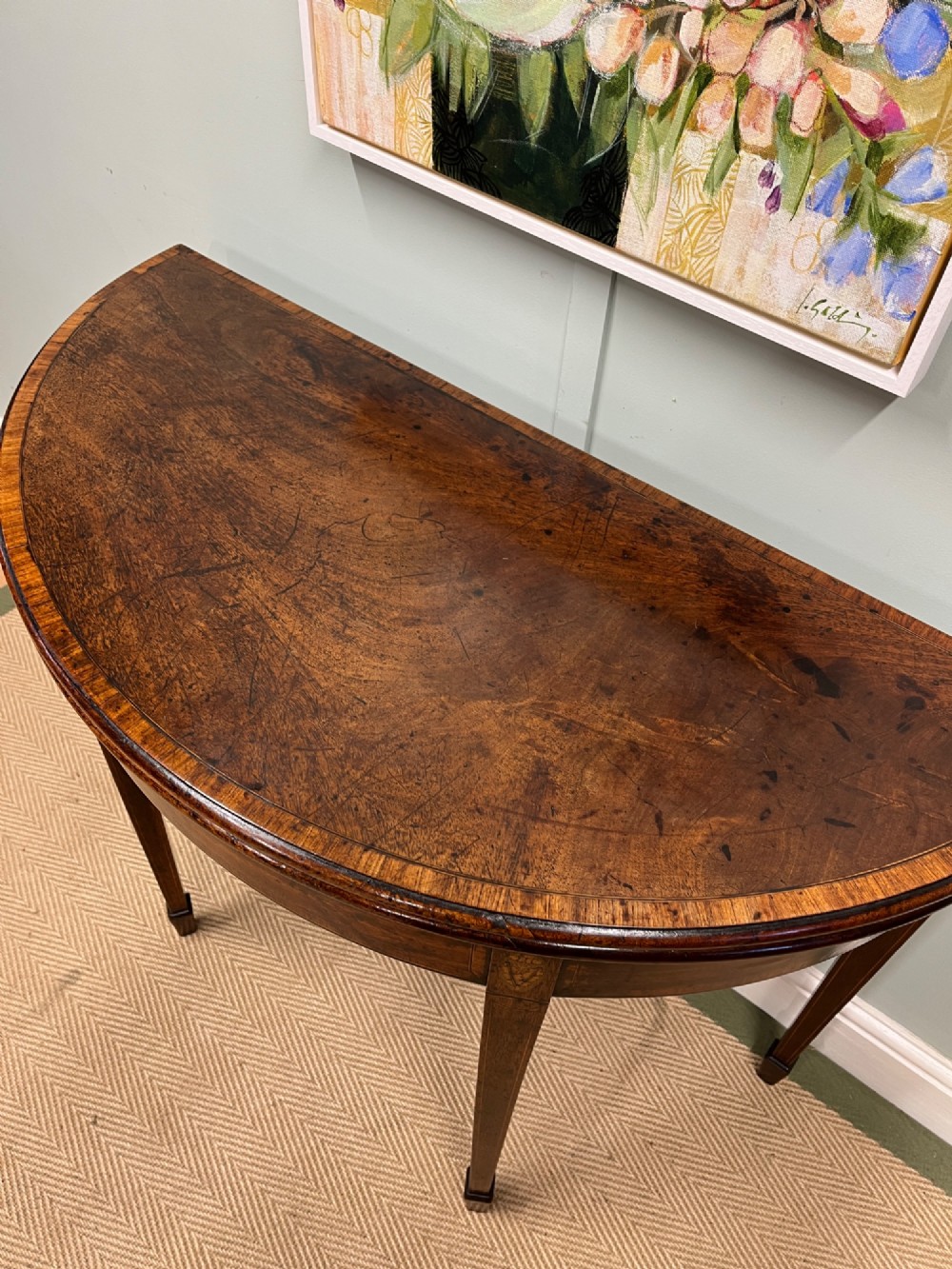 A Georgian mahogany demilune tea table featuring wood stringing and four tapered square legs. View V