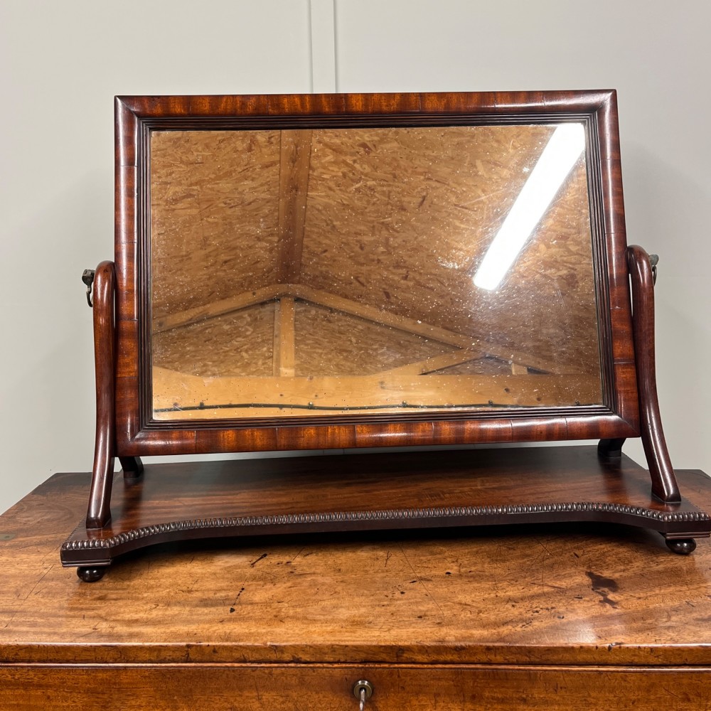 A 19th-century rectangular flame mahogany toilet mirror with a swivelling frame resting on a shaped platform base with carved edging.