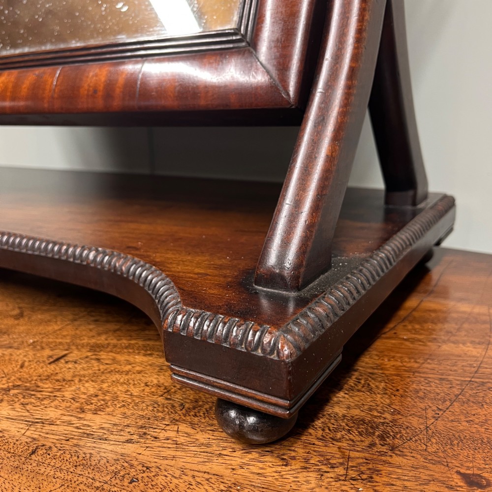 A 19th-century rectangular flame mahogany toilet mirror with a swivelling frame resting on a shaped platform base with carved edging. View II