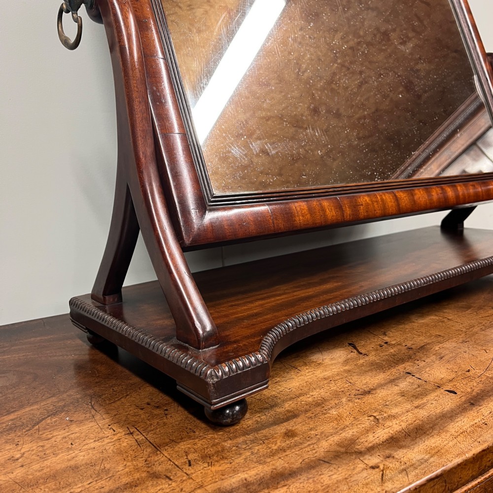 A 19th-century rectangular flame mahogany toilet mirror with a swivelling frame resting on a shaped platform base with carved edging. View IV