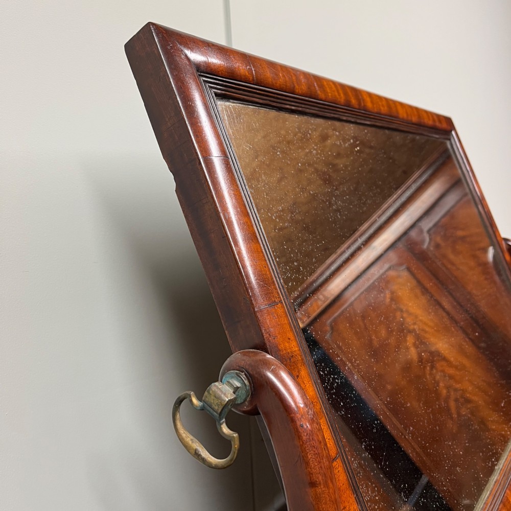 A 19th-century rectangular flame mahogany toilet mirror with a swivelling frame resting on a shaped platform base with carved edging. View V