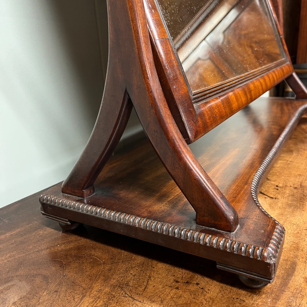 A 19th-century rectangular flame mahogany toilet mirror with a swivelling frame resting on a shaped platform base with carved edging. View VI