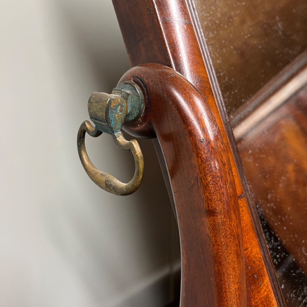 A 19th-century rectangular flame mahogany toilet mirror with a swivelling frame resting on a shaped platform base with carved edging. View X