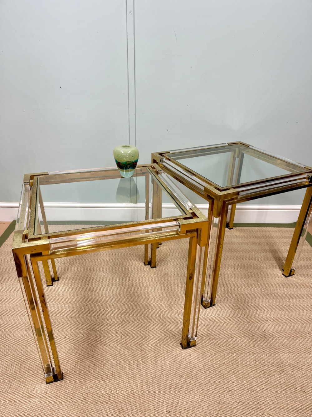 A pair of square side tables featuring brass frames, clear lucite corner inserts, and glass tops.