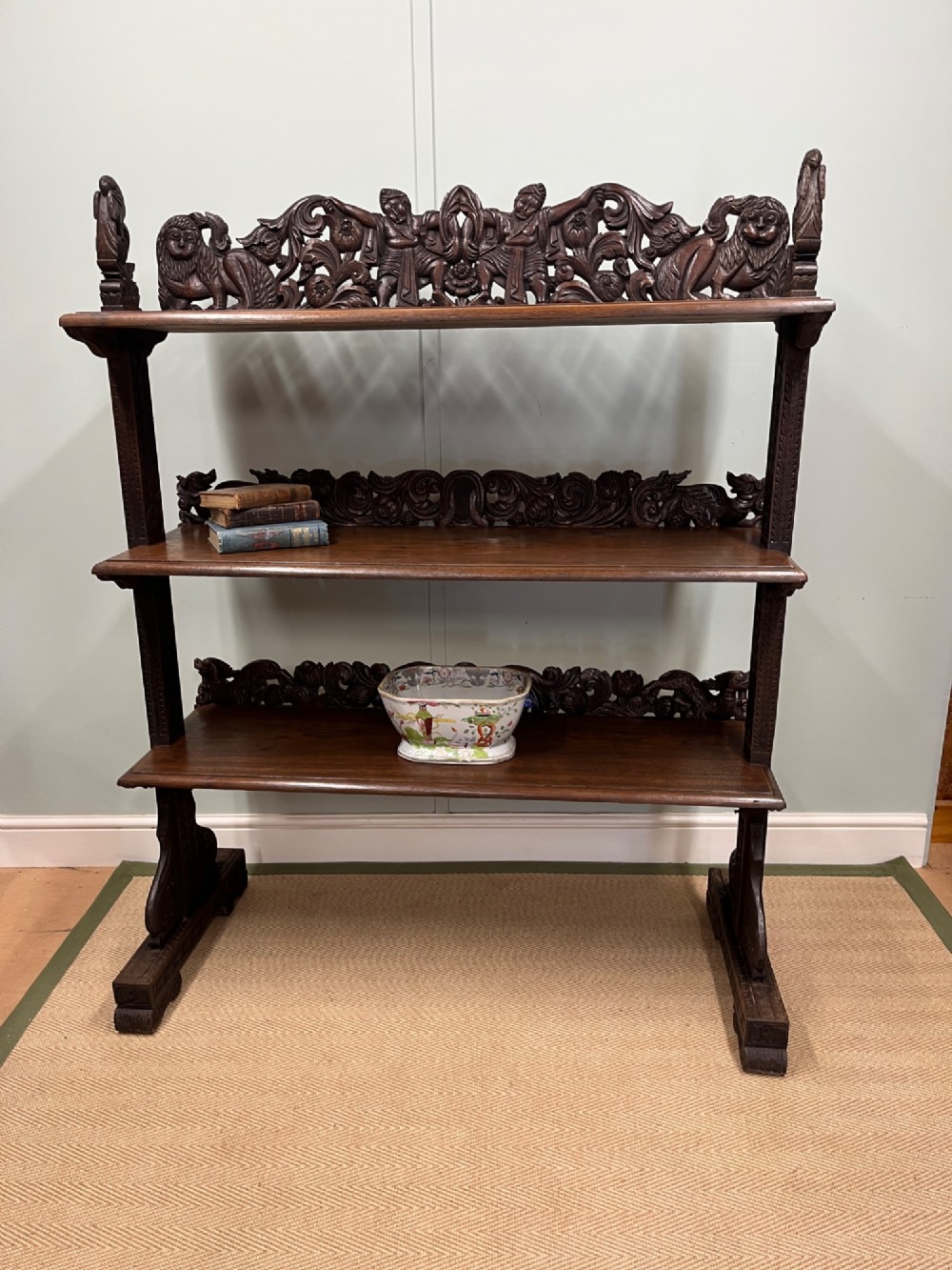 A 19th-century carved dark teak three-tier buffet featuring relief-carved backboard galleries with figurative motifs, supported on carved uprights and trestle feet.