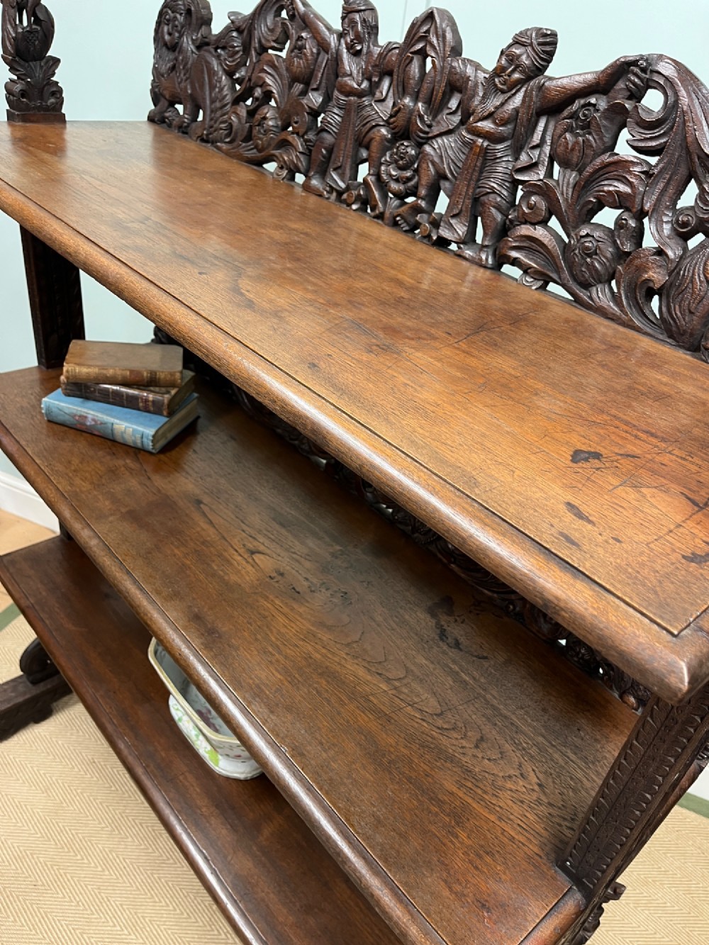 A 19th-century carved dark teak three-tier buffet featuring relief-carved backboard galleries with figurative motifs, supported on carved uprights and trestle feet. View V
